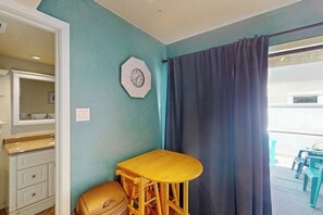 A room with a teal wall, a wooden table with a chair, a clock, and a window with curtains. - Sand Dollar #5 - Canal-Front, Pool & Pier (Corpus Christi)