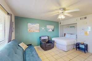 A room with a bed, a chair, a sofa, a ceiling fan, and wall art. - Sand Dollar #5 - Canal-Front, Pool & Pier (Corpus Christi)
