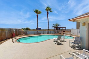 A swimming pool with lounge chairs, palm trees, and a wooden fence. - Sand Dollar #5 - Canal-Front, Pool & Pier (Corpus Christi)