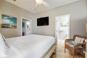 Ein Schlafzimmer mit einem großen Bett, einem an der Wand befestigten Fernseher und einem Korbstuhl.