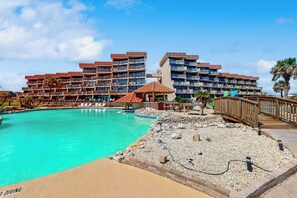 A hotel with multiple balconies, a swimming pool, and a wooden bridge. - Mayan Princess - Howdy Lobster (Port Aransas)