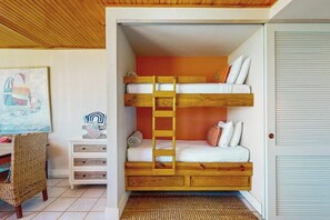 Una cama litera con escalera, un escritorio con cajones, una silla de mimbre y un cuadro en la pared.