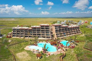 A multi-story hotel with a pool area, surrounded by a fence and palm trees. - Mayan Princess - Howdy Lobster (Port Aransas)