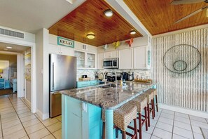 A kitchen with a central island, white cabinets, a stainless steel refrigerator, and a microwave. - Mayan Princess - Howdy Lobster (Port Aransas)