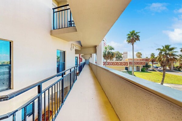Un balcón con barandilla metálica, vista despejada a una palmera y un edificio con fachada ornamentada al fondo.