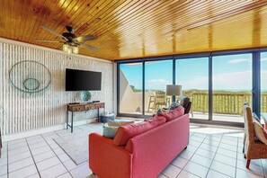 A modern living room with a large TV, a red sofa, and a balcony with a view. - Mayan Princess - Howdy Lobster (Port Aransas)