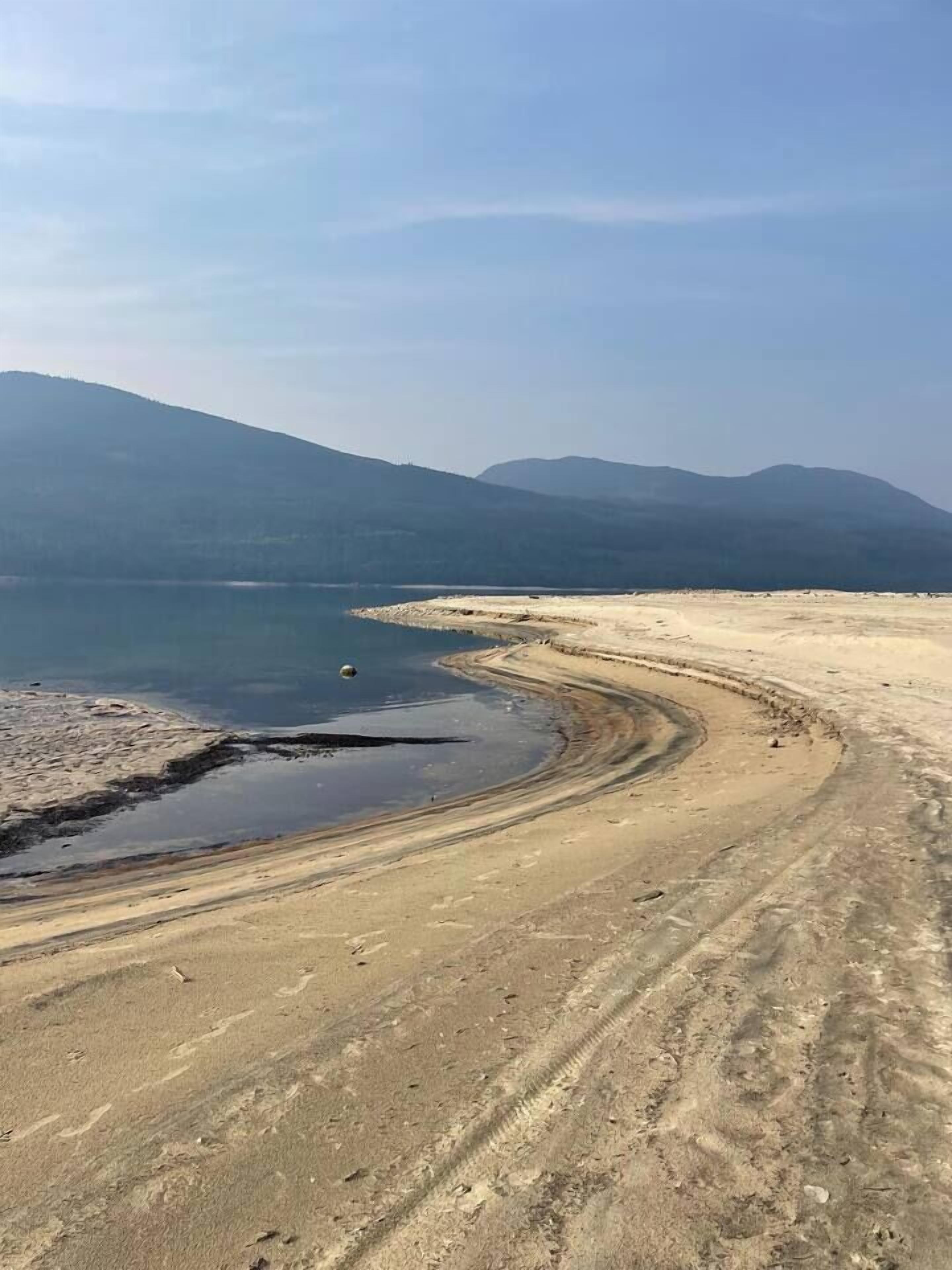 A panoramic view of a coastal landscape with a curved shoreline, a body of water, and distant mountains.
