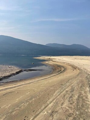 Vista panorámica de un paisaje costero con una línea de costa curva, una masa de agua y montañas distantes.