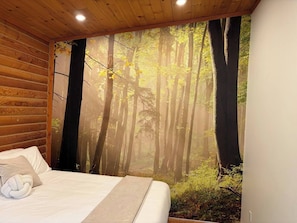 A bedroom with a bed, a wooden headboard, and a forest mural on the wall.