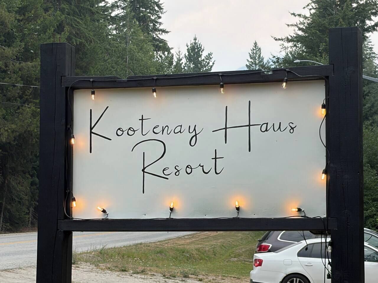 A sign for Kootenay Haus Resort with a simple, clear font on a white background, surrounded by a black frame and small lights.