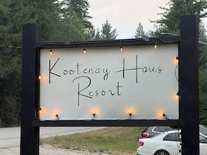 Señal para Kootenay Haus Resort con una tipografía clara y sencilla sobre fondo blanco, rodeada de un marco negro y pequeñas luces.