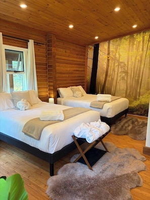 Un dormitorio tipo cabaña de madera con dos camas, un ventanal grande y un mural con un bosque.