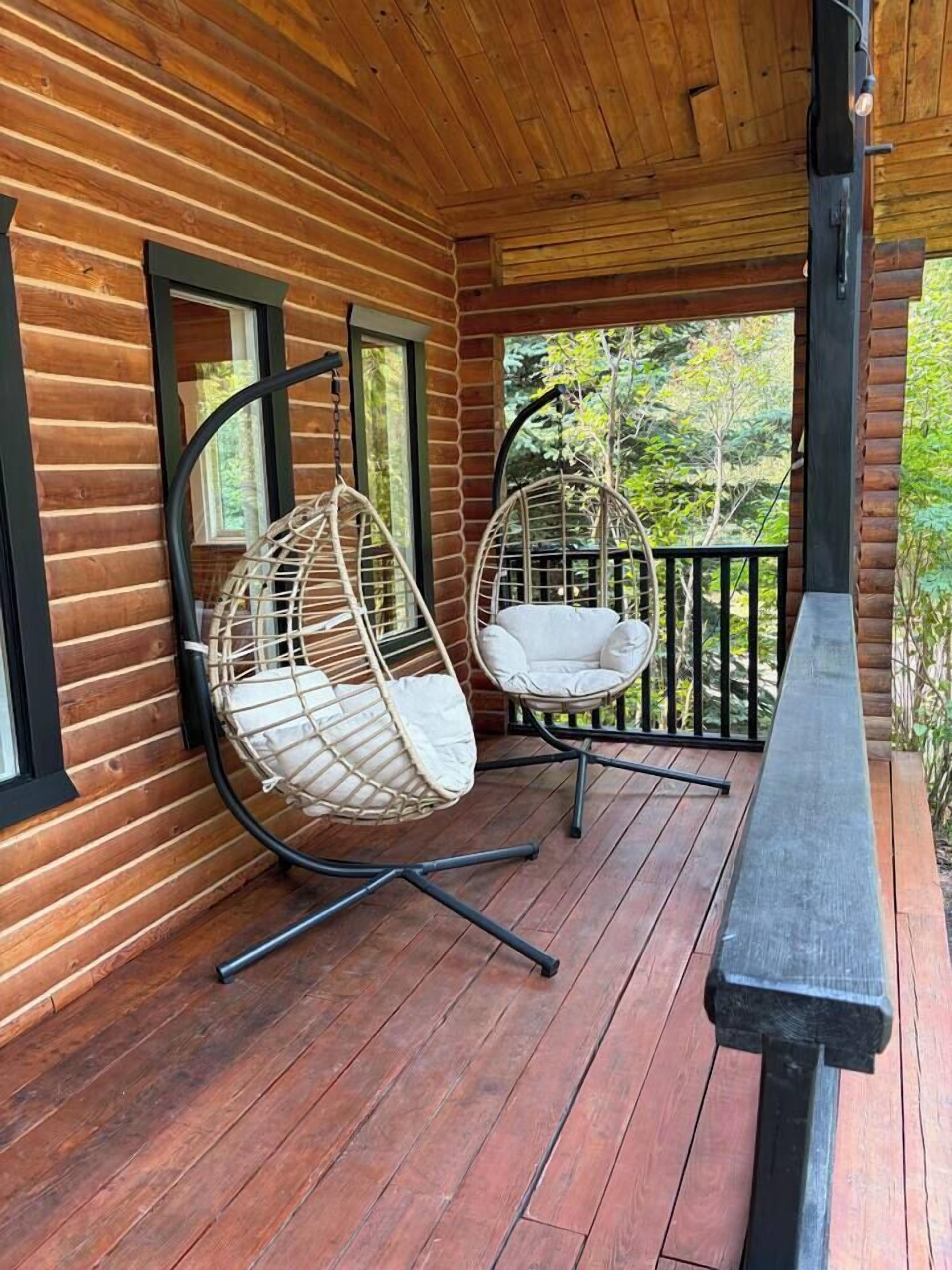 A wooden cabin with a porch, two hanging chairs, and a bench.