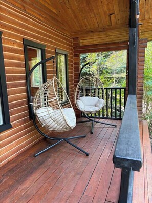 Una cabaña de madera con un porche, dos sillones colgantes y un banco.