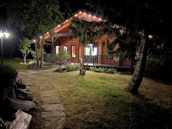 A wooden cabin with a porch, surrounded by a stone pathway and a grassy yard.
