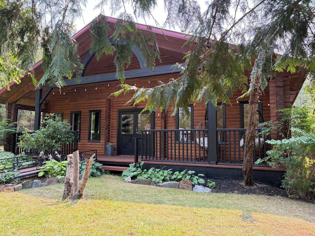A wooden cabin with a porch, surrounded by a garden with various plants and a tree stump.