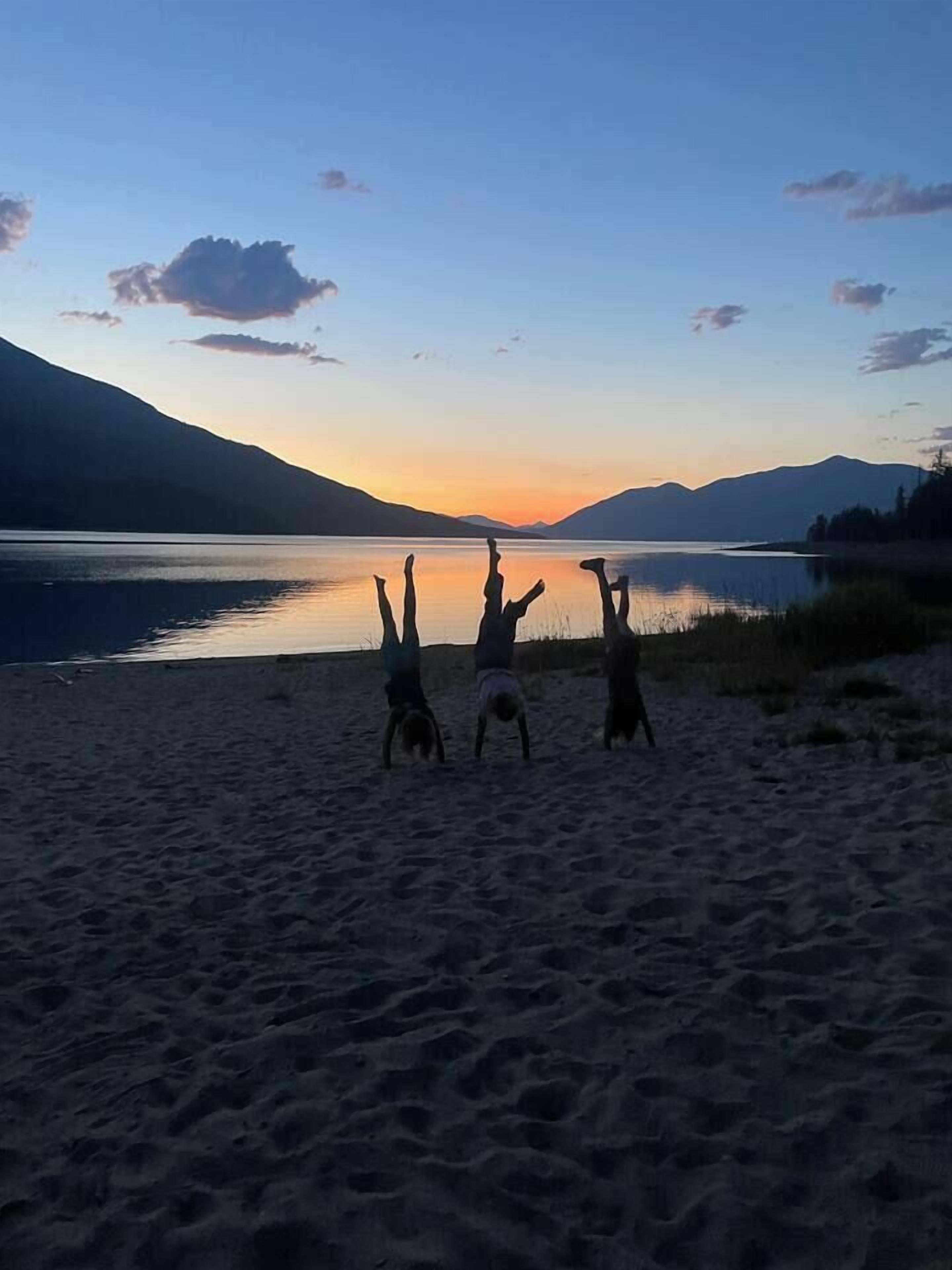 A beach with three people doing handstands facing the sunset.