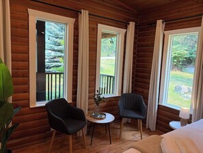 A log cabin room with two chairs, a small table, and a bed.