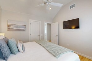 A bedroom with a bed, a ceiling fan, a television, and a door leading to another room. - Beach Bummz Bungalow (Port Aransas)