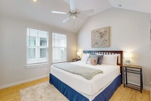 A bedroom with a bed, two bedside tables, a ceiling fan, and a window with blinds. - Beach Bummz Bungalow (Port Aransas)