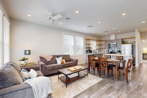 A modern living room with a sofa, coffee table, and dining area with chairs. - Beach Bummz Bungalow (Port Aransas)