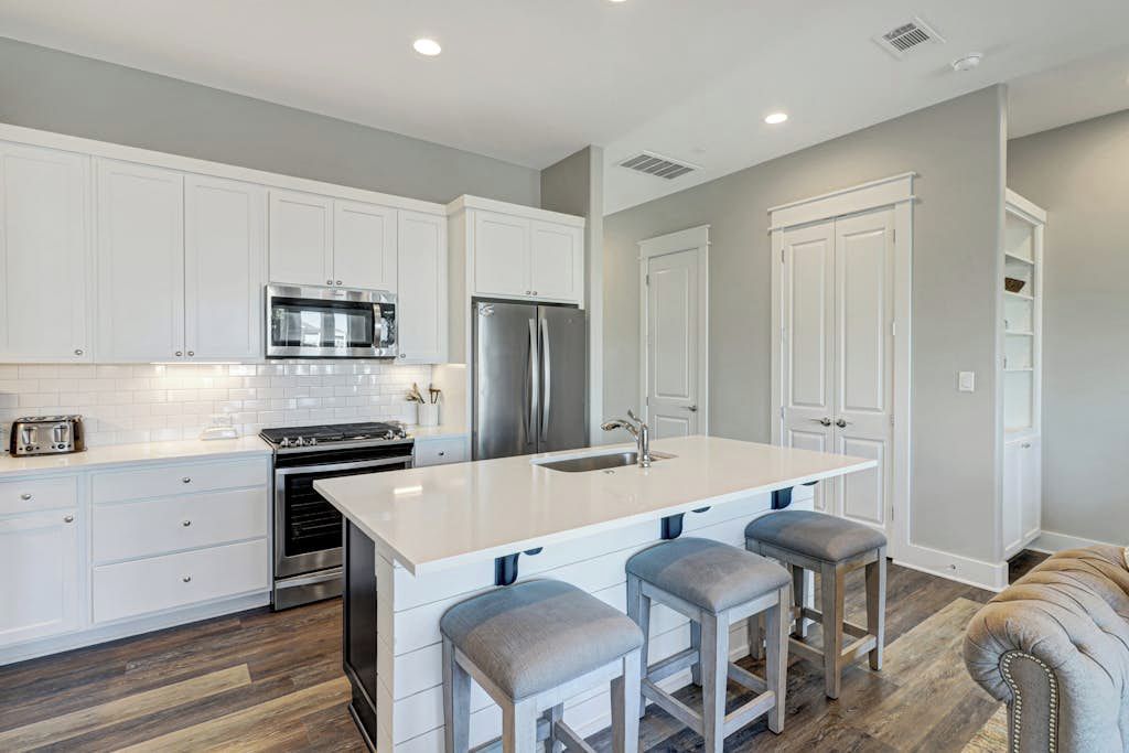 A modern kitchen with white cabinetry, stainless steel appliances, and a central island with bar stools.