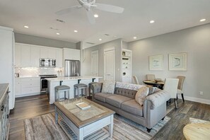 Eine moderne Küche mit weißen Schränken, Edelstahlgeräten und einem Essbereich mit grauem Sofa und Couchtisch.