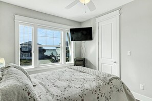 Ein Schlafzimmer mit einem Bett, einem an der Wand montierten Fernseher und einem Fenster mit Blick auf Häuser.