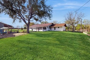 A house with a large lawn, a covered porch, and a tree in the foreground. - R&R Acres - 17 Acres, Wildlife & Grill (Aransas Pass)