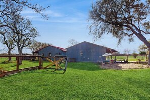 A barn and a small house with a red roof, surrounded by a fenced area with a swing set and picnic table. - R&R Acres - 17 Acres, Wildlife & Grill (Aransas Pass)