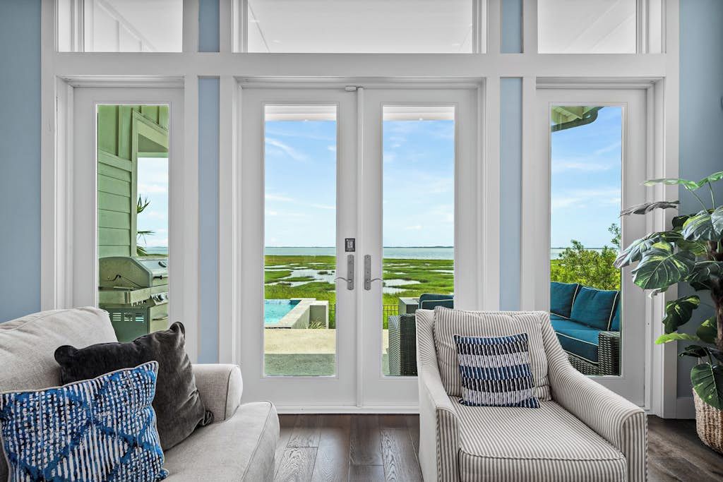 A room with a view of a swimming pool and greenery, featuring a sofa and a chair with patterned cushions.