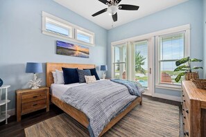 A bedroom with a bed, nightstands, a ceiling fan, and a window with blinds. - Bay Reserve - Bayfront, Private Heated Pool (Rockport)