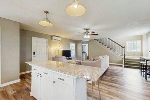 A spacious kitchen with a central island, a dining area with a table and chairs, a staircase leading to another level, and a living room with a sofa and television. - Sandy Toes - Fenced Yard, Blocks to the Beach (Rockport)