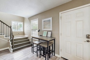 A room with a staircase, a desk with two chairs, a framed picture, and a white door. - Sandy Toes - Fenced Yard, Blocks to the Beach (Rockport)