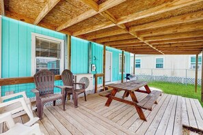 A covered outdoor area with wooden flooring, a picnic table, and Adirondack chairs. - Sandy Toes - Fenced Yard, Blocks to the Beach (Rockport)
