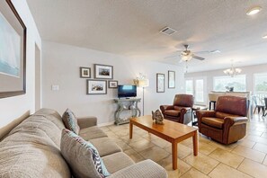 A living room with a sofa, two armchairs, a coffee table, a television, and framed pictures on the wall. - Copano Bayfront Haven (Rockport)
