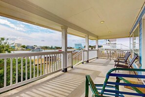 A covered outdoor area with a railing, chairs, and a view of the surrounding landscape. - Copano Bayfront Haven (Rockport)
