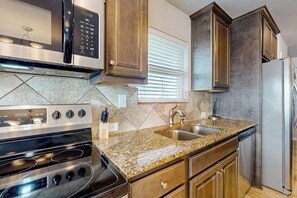 A kitchen with a stainless steel stove, a microwave, a sink, and wooden cabinets. - Copano Bayfront Haven (Rockport)
