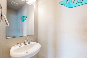 Un baño con lavamanos blanco, un espejo y un perchero para toallas.