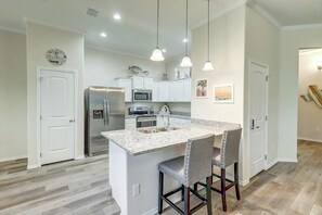 A modern kitchen with white cabinetry, a stainless steel refrigerator, a microwave, and a sink. There are two pendant lights hanging above the island, and a clock on the wall. - Rockport Relaxation - Shared Pool, Golf Nearby (Rockport)