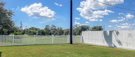 A grassy outdoor area with a white fence, a utility pole, and a white building in the background.