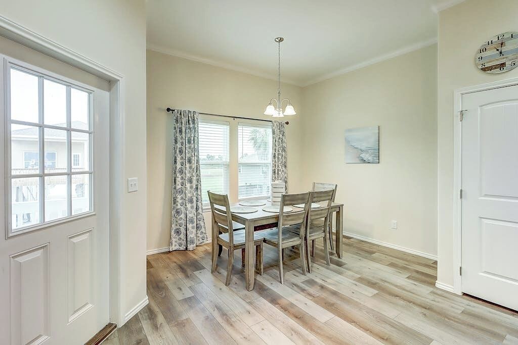 A dining area with a wooden table and chairs, a chandelier, and a window with curtains.