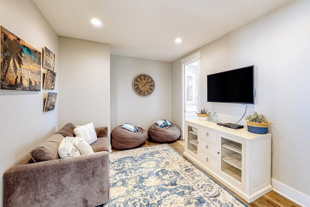 Un salon comprenant un canapé, des fauteuils poire, un tapis à motifs, une horloge, un téléviseur et un meuble contenant des objets décoratifs.