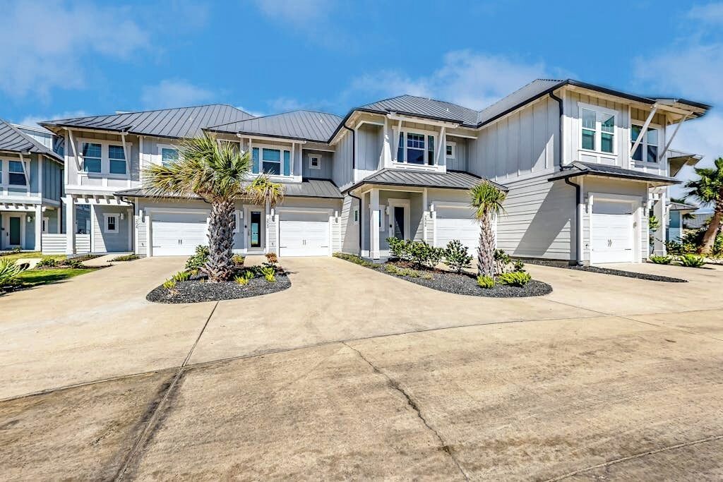 Un immeuble résidentiel doté d’une allée, de plusieurs garages et d’espaces paysagers agrémentés de palmiers.