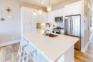 A modern kitchen with white cabinetry, a stainless steel refrigerator, a microwave, and a large island with stools.