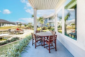 A covered patio with a table and chairs, overlooking a residential area with houses and a body of water.