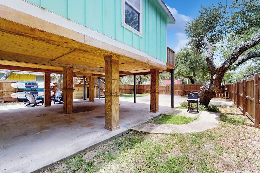 Ein überdachter Patio-Bereich mit Holzsäulen, einem Betonboden und einem umzäunten Hinterhof.