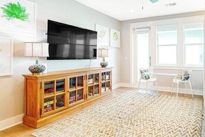 Ein Wohnzimmer mit Flachbildfernseher an der Wand, einer Holzvitrine mit Glastüren, einem gemusterten Teppich und einem kleinen Tisch mit Stühlen.