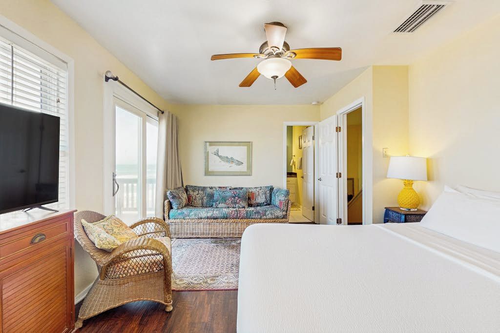A bedroom with a bed, a television, a ceiling fan, a sofa, and a window.