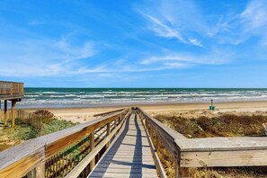 A wooden boardwalk leading to a beach with the ocean in the background. - Lost Colony Make A Splash (Port Aransas)